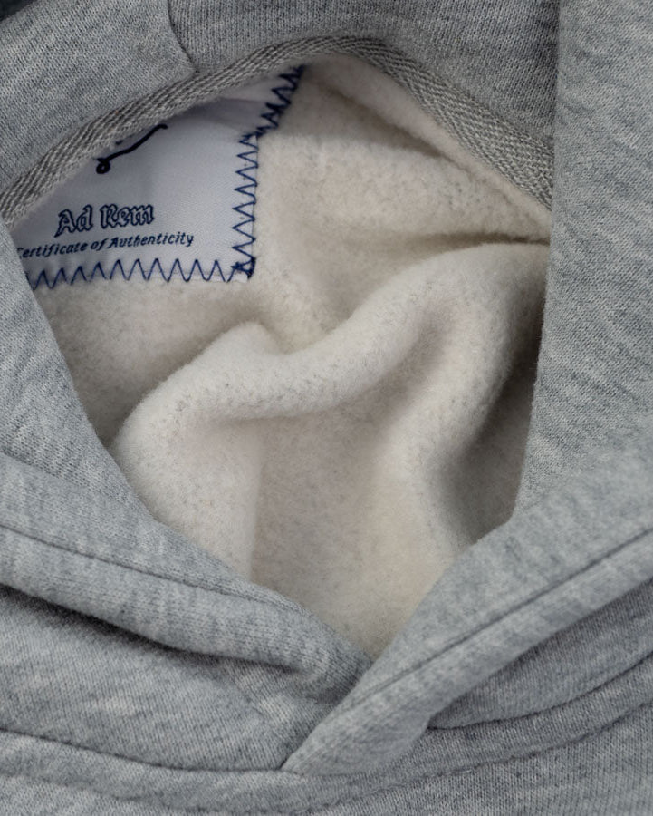 Close-up of a gray hooded sweatshirt showing the interior lining and a visible inner label that reads 'Ad Rem' and 'Certification of Authenticity'.
